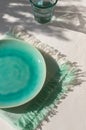 Empty turquoise ceramic plate with napkin with fringe on white plaster background with leaves shadows. Royalty Free Stock Photo