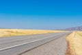 Empty two way road navigates between scenic agriculture fields toward hills under blue sky