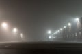 Empty urban car parking and streetlights at foggy night. Old Industrial brick building and lanterns on lonely street Royalty Free Stock Photo