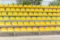 Empty vacant stadium stands, chairs, plastic yellow arena spectator seats on a small football soccer field, daytime, pan, nobody