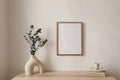 Empty vertical picture frame mockup hanging on beige wall. Cup of coffee, books on wooden table. Vase with silver