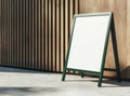 Empty vertical poster board with green frame placed outdoors by wooden wall Royalty Free Stock Photo
