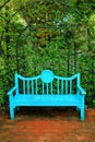 Empty vibrant turquoise blue wooden bench on terracotta brick path in green garden Royalty Free Stock Photo