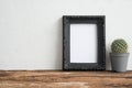 Empty vintage black photo frame on old wooden table with cactus pot over white concrete wall background copy space. Creative idea Royalty Free Stock Photo