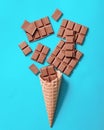 An empty waffle cone sits on a blue background, surrounded by scattered pieces of chocolate bar, creating a playful and tempting