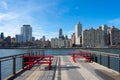 Waterfront along the East River at Roosevelt Island with Red Picnic Tables and looking towards the Upper East Side Skyline of New