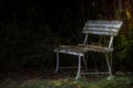 Empty weathered white bench abandoned in the shade of the trees in a park, while the first spring light falls through the branches Royalty Free Stock Photo