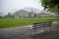 Empty wet metal bench in front of a green field at Interlaken with foggy mountain and buildings background