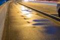 Empty wet sidewalk with rain puddles, road and side road parking lots. Coming cars lighten area. Night city life. Selective focus Royalty Free Stock Photo