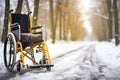 An empty wheelchair stands on the road in a snowy winter park. Difficulty of movement of disabled people