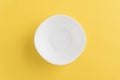 Empty white bowl on yellow background, top-down view