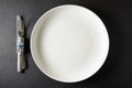 Empty white ceramic plate with cutlery wrapped in hundred dollar bill on black stone table. Top view with copy space Royalty Free Stock Photo