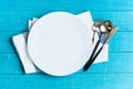 Empty white ceramic round plate with table cloth,knife,spoon and fork on blue wooden background Royalty Free Stock Photo