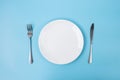 Empty white ceramics plate with knife and fork on blue background. dining and kitchenware concept Royalty Free Stock Photo