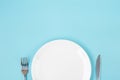 Empty white ceramics plate with knife and fork on blue background. dining and kitchenware concept Royalty Free Stock Photo