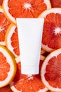 Empty white cream tube mockup unbranded lying on a grapefruit slices. Top view. Vertical