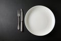 Empty white dinner plate and cutlery on a black stone table. Top view with copy space Royalty Free Stock Photo