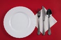 Empty white dinner plate with silver fork and Dessert Tablespoon, isolated on red tablecloth background with copy space. Table Set Royalty Free Stock Photo