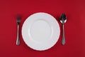 Empty white dinner plate with silver fork and Dessert Tablespoon isolated on red tablecloth background with copy space. Table Set Royalty Free Stock Photo
