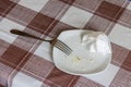 empty white dish with leftovers of eaten food, crumpled table-napkin and steel fork