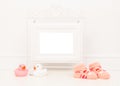 Empty white picture frame with space for text or wishes in a white living room setting with pink baby sock and pink and white rubb