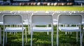 Empty white plastic chairs on green grass field with blurred background of spectators Royalty Free Stock Photo