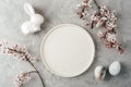 Empty white plate with ceramic bunny, speckled eggs and cherry blossoms on grey background. Easter concept. Top view Royalty Free Stock Photo