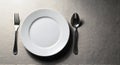 Empty white plate with a fork and spoon set on a textured gray surface, symbolizing a meal, diet, or waiting Royalty Free Stock Photo