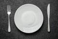 Empty white plate with knife and fork on black table. Royalty Free Stock Photo