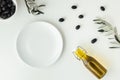 Empty white plate next to white bowl full of black olives and a bottle of olive oil and leaves. White background. Bottle of cold Royalty Free Stock Photo