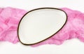 Empty white plate on pink folded cotton textile on white painted wooden table