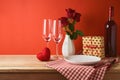 Empty white plate with wine glasses, heart shape and rose flowers on wooden table over red background. Valentine`s day romantic Royalty Free Stock Photo