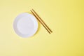 Empty white plate with a wooden chopsticks on a yellow background Royalty Free Stock Photo