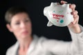 Empty white porcelain piggy bank held upside down by woman in business white shirt, on black background. Concept for