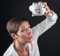 Empty white porcelain piggy bank held upside down by woman in business white shirt, on black background. Concept for
