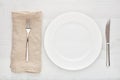 Empty white round ceramic plate, fork, knife and napkin on white wooden table. Royalty Free Stock Photo