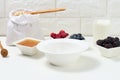 Empty white round ceramic plate, oatmeal and fruit for cooking porridge on a white table