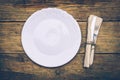 Empty white rustic plate on old wooden background with knife, fork and napkin. Rustic food concept. Royalty Free Stock Photo