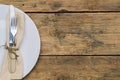 Empty white rustic plate on old wooden background with knife, fork and napkin. Rustic food concept. Royalty Free Stock Photo