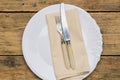 Empty white rustic plate on old wooden background with knife, fork and napkin. Rustic food concept. Royalty Free Stock Photo