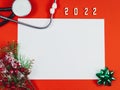 Empty white sheet, stethoscope, fir branches, ribbon flower and wooden numbers 2022 on red