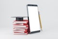 Empty white smartphone with book stack and graduation cap on light background. Online education and training concept. Mock up Royalty Free Stock Photo