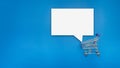Empty white speech bubble on a mini shopping trolley over blue background Royalty Free Stock Photo