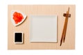 Empty white square plate with chopsticks for sushi and soy sauce, ginger on brown sushi mat background. Top view with copy space Royalty Free Stock Photo