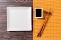 Empty white square plate with chopsticks for sushi and soy sauce on wooden background. Top view with copy space Royalty Free Stock Photo