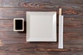 Empty white square plate with chopsticks for sushi and soy sauce on wooden background. Top view with copy space Royalty Free Stock Photo