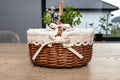 An empty wicker Easter basket, decorated with boxwood and catkins, standing on a table.