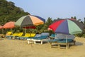 Empty wooden beach loungers with mattresses under bright large multi-colored sun umbrellas on the sand against the backdrop of the