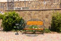 Empty wooden bench with an ashtray on a sunny summer day with a cactus on the background of a stone wall. Mediterranean style Royalty Free Stock Photo