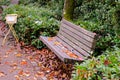 An empty wooden bench in autumn park with colorful trees background. The bench is surrounded by red leaves Royalty Free Stock Photo